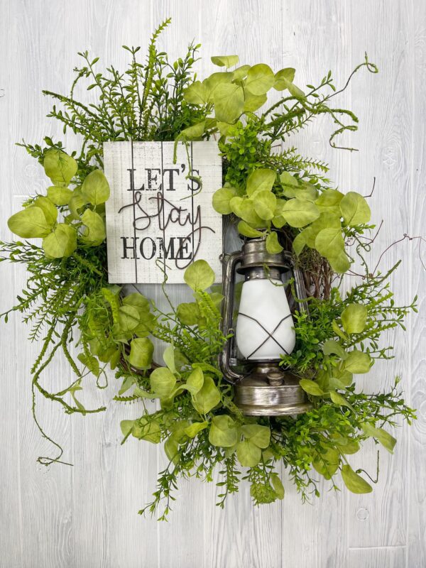 Let's stay home sign and lantern on a wreath with greenery