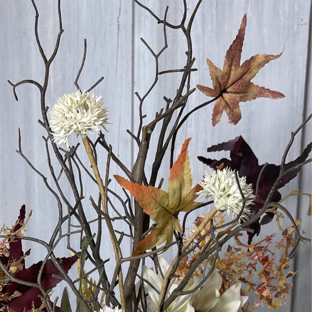 Layered greenery and rustic branch in fall centerpiece.
