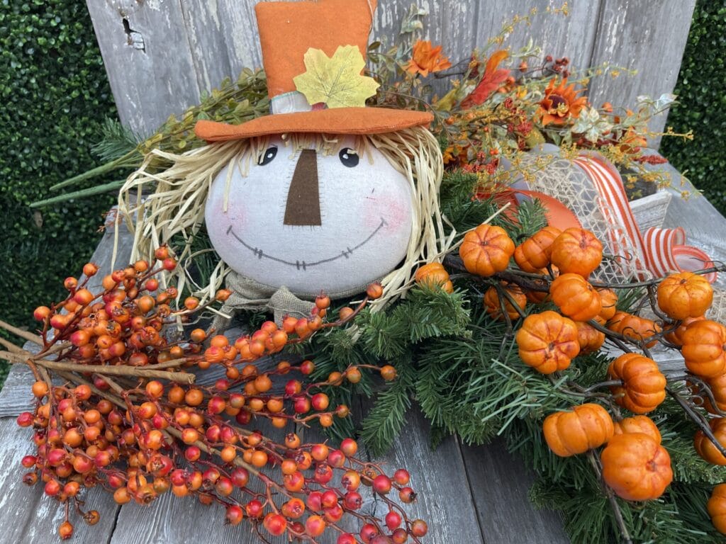 Fall scarecrow with orange pumpkins berries greenery and autumn ribbon
