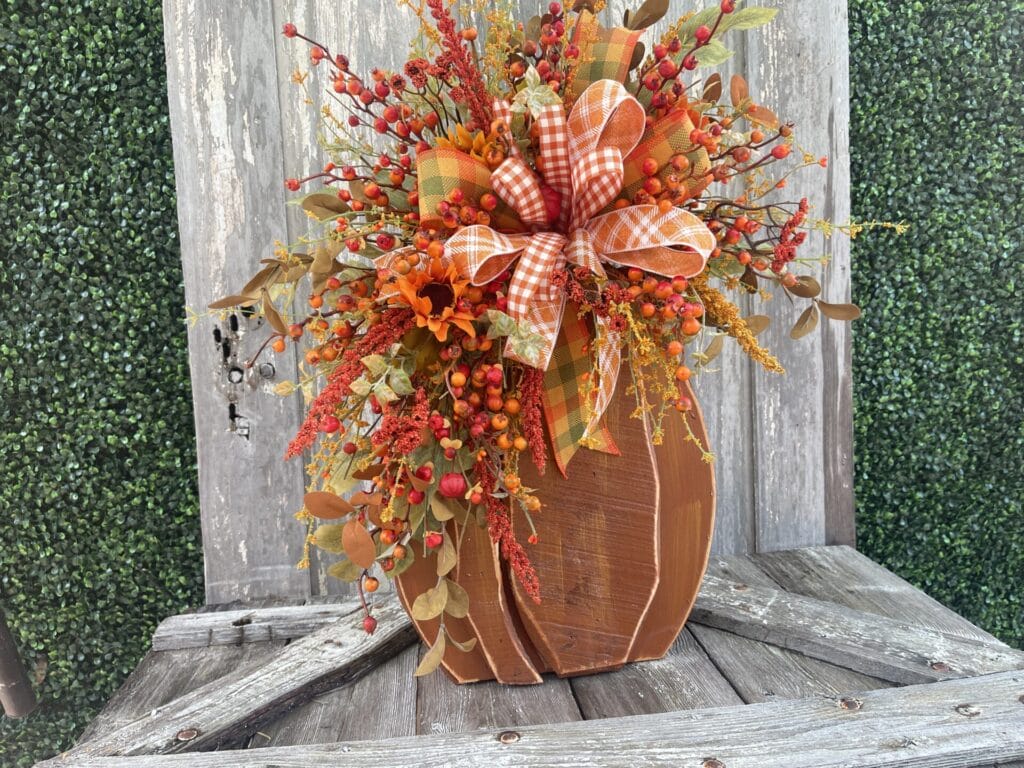 Wood pumpkin fall floral arrangement with orange berries, sunflowers and plaid ribbon
