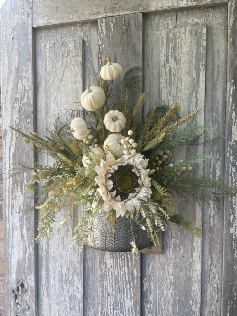 Neutral fall wall floral arrangement with cream pumpkins, sunflower and wispy greenery